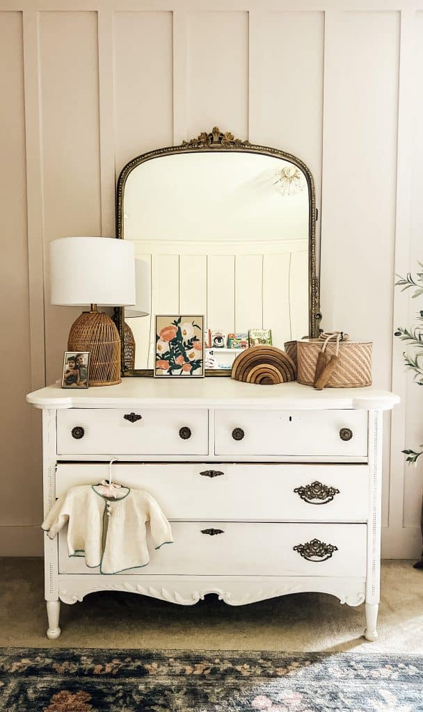 Chippy white dresser with wooden toys on top and gleaming primrose Anthropologie mirror